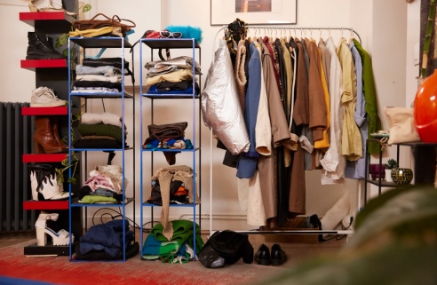 Vêtements de seconde main soigneusement rangés sur des portants et étagères, mêlant styles et couleurs, avec des chaussures et accessoires organisés.