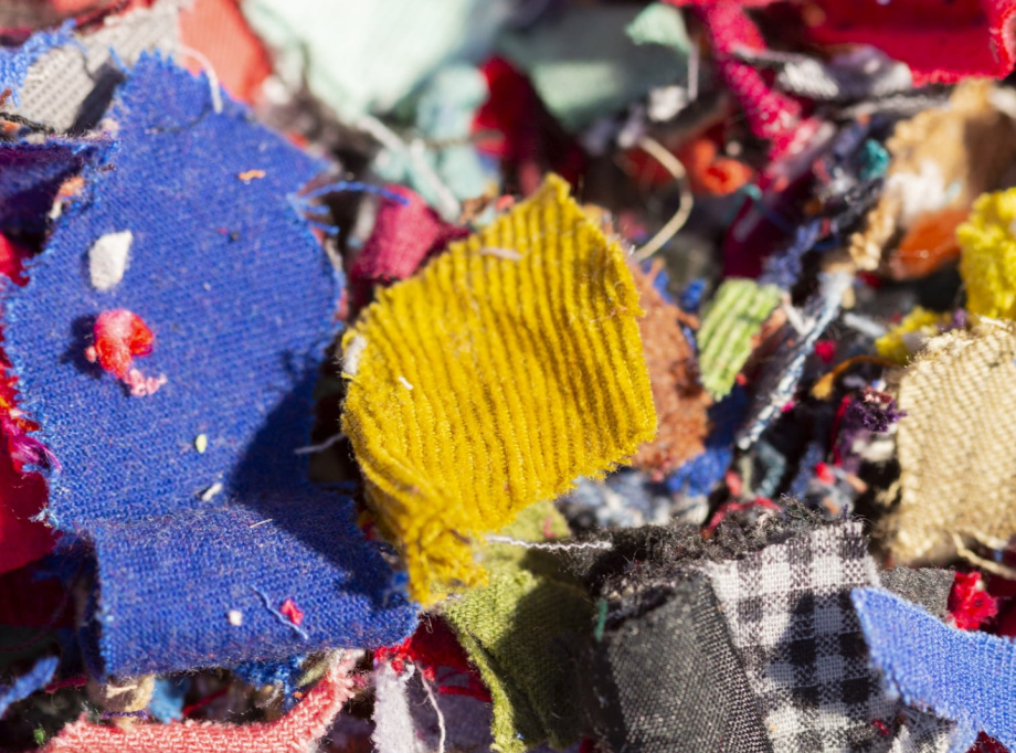 Un tas de chutes de tissus colorés de différentes textures et motifs, comprenant des morceaux de bleu, rouge, jaune, noir et blanc, avec certains présentant des motifs à carreaux ou en maille.