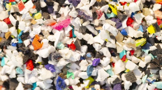 Un amas de petits fragments broyés de matières plastiques et textiles multicolores, composé de morceaux blancs, noirs, rouges, bleus, jaunes et autres couleurs.