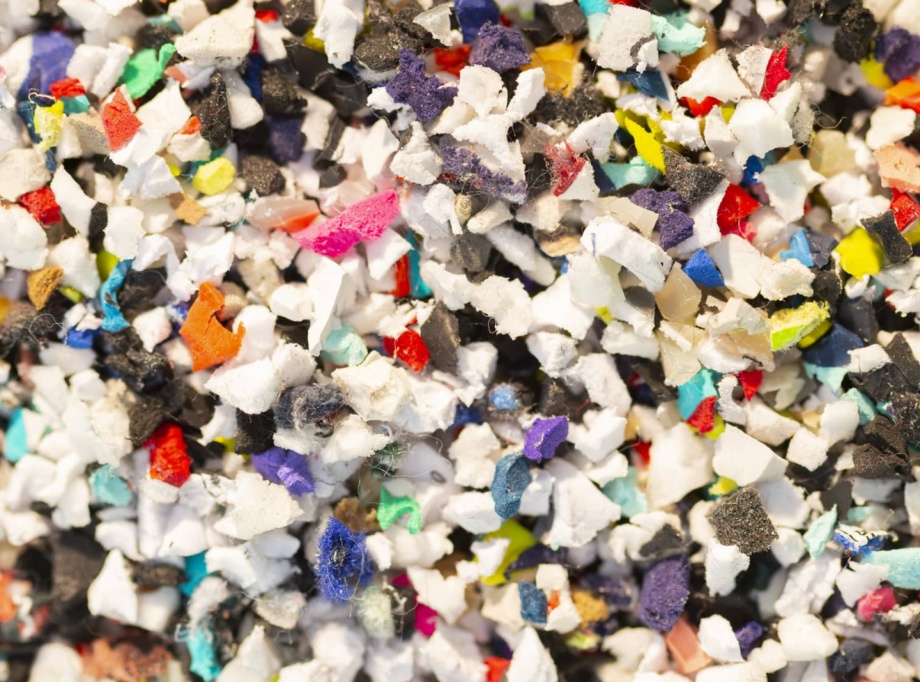 Un amas de petits fragments broyés de matières plastiques et textiles multicolores, composé de morceaux blancs, noirs, rouges, bleus, jaunes et autres couleurs.