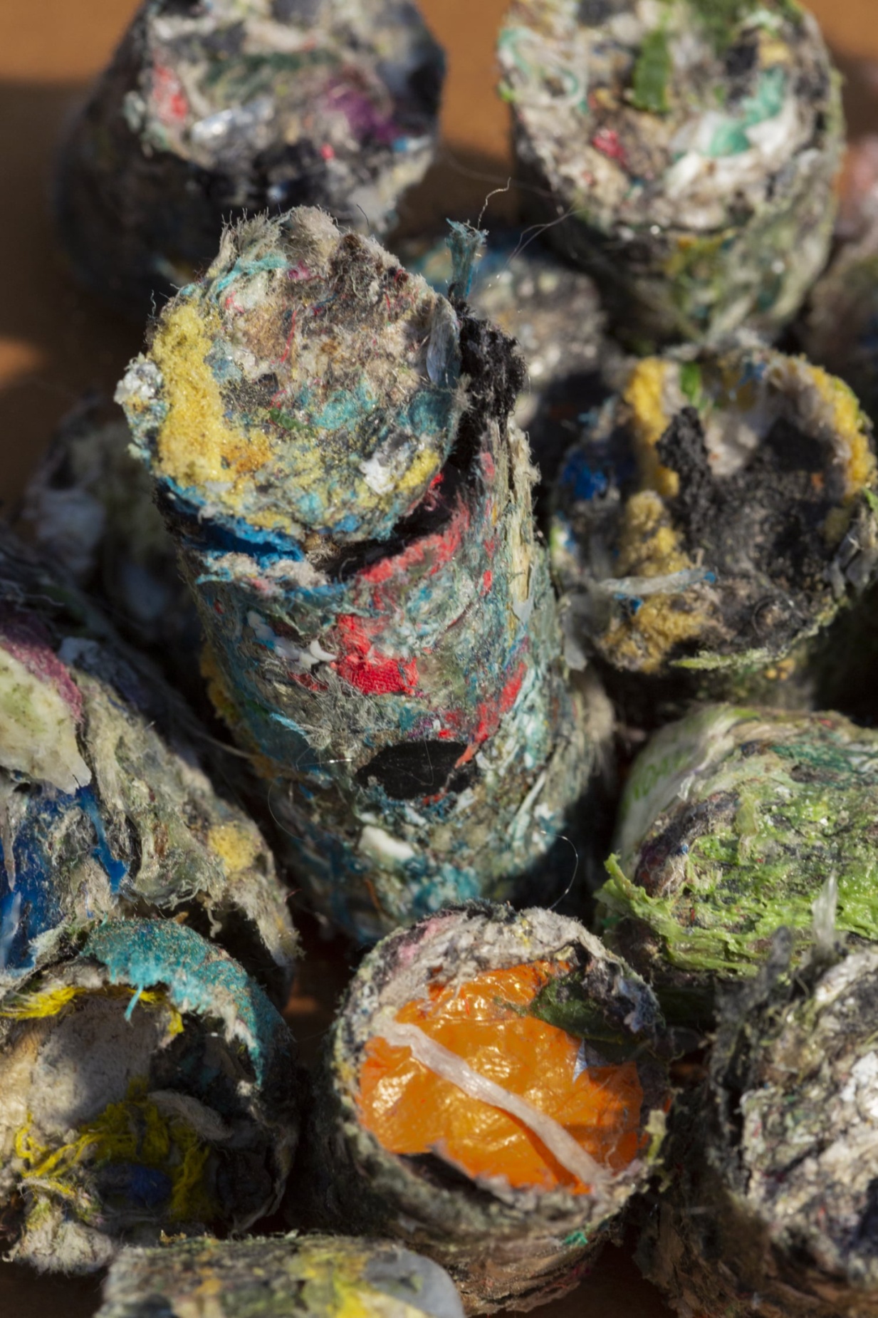 Des cylindres compressés composés de déchets textiles et plastiques colorés, avec des morceaux visibles de tissu, de fibres et de films plastiques.