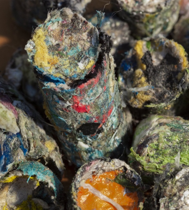 Des cylindres compressés composés de déchets textiles et plastiques colorés, avec des morceaux visibles de tissu, de fibres et de films plastiques.