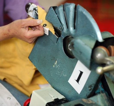 Une personne utilise une machine industrielle en métal bleu avec un mécanisme rotatif pour retirer un bouton pression d'un tissu jaune. La machine est étiquetée avec le chiffre "1".