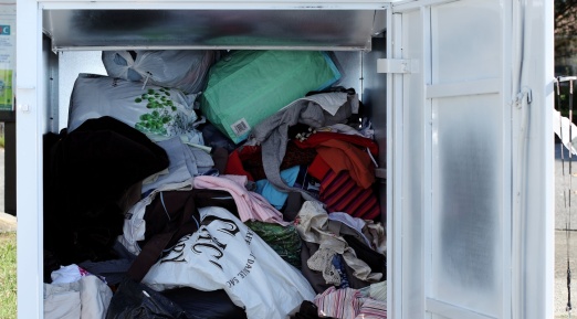 Un conteneur de collecte de vêtements avec sa porte ouverte, rempli de dons textiles en vrac.