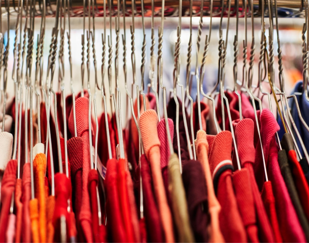 Portant de vêtements : rangée de cintres en métal tenant des habits rouges et colorés.