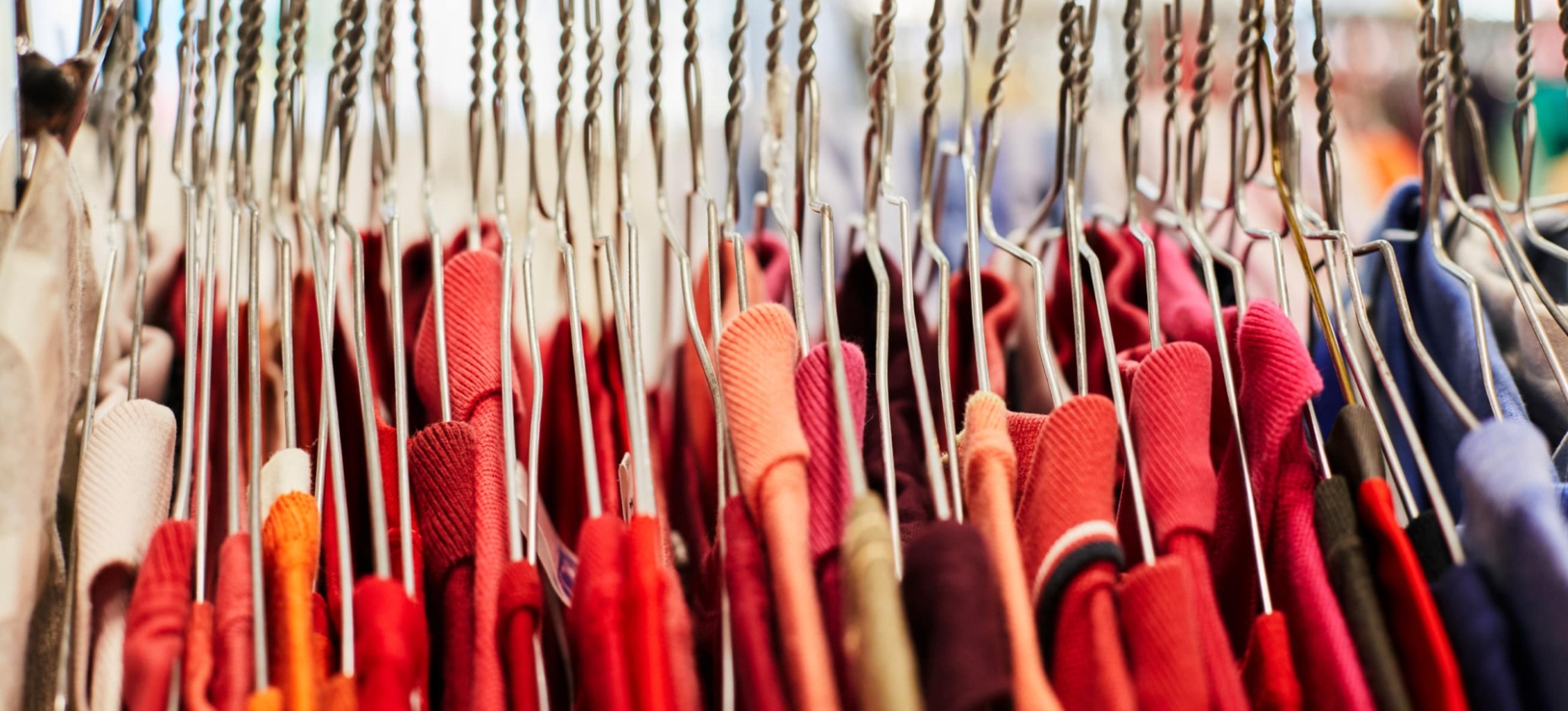 Portant de vêtements : rangée de cintres en métal tenant des habits rouges et colorés.