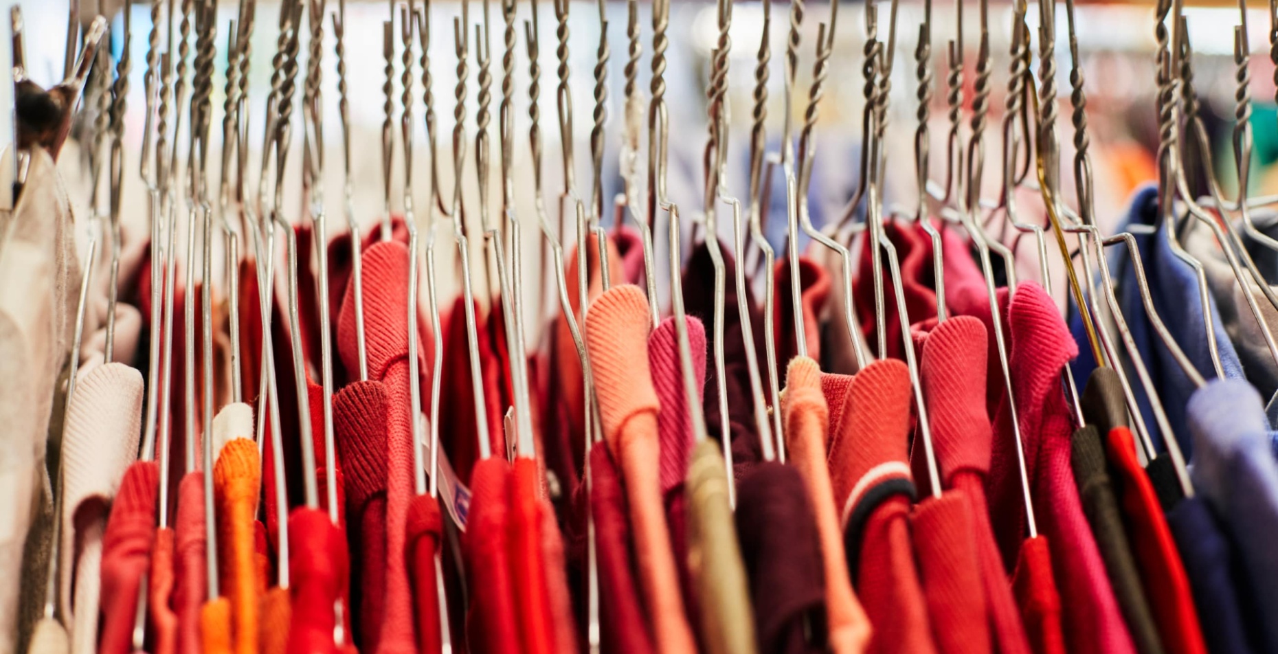 Portant de vêtements : rangée de cintres en métal tenant des habits rouges et colorés.