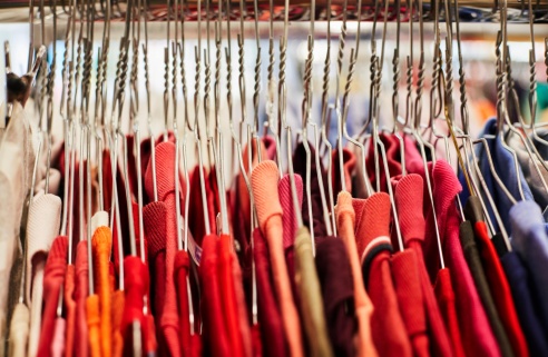 Portant de vêtements : rangée de cintres en métal tenant des habits rouges et colorés.