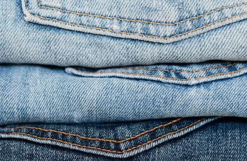 Pile de jeans de différentes teintes de bleu, soigneusement empilés, mettant en valeur la texture et les coutures du denim.