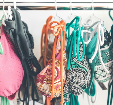 L’image montre un portant rempli de maillots de bain colorés suspendus à des cintres. Les motifs variés et les couleurs vives suggèrent un mélange de styles et de designs, probablement dans un magasin ou un espace de seconde main. L’ensemble dégage une ambiance estivale et dynamique.