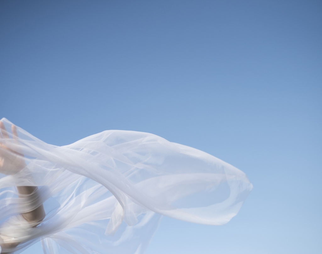 Voile blanc flottant au vent sur fond de ciel bleu, avec une main en mouvement.