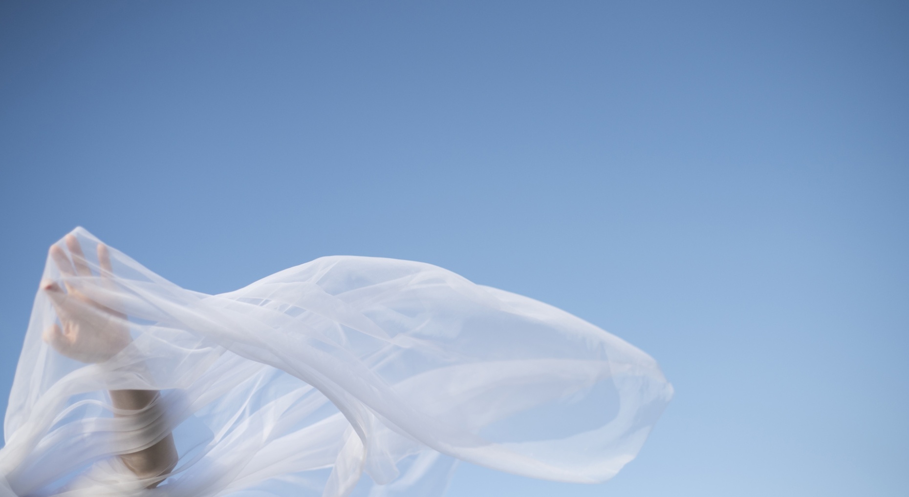 Voile blanc flottant au vent sur fond de ciel bleu, avec une main en mouvement.