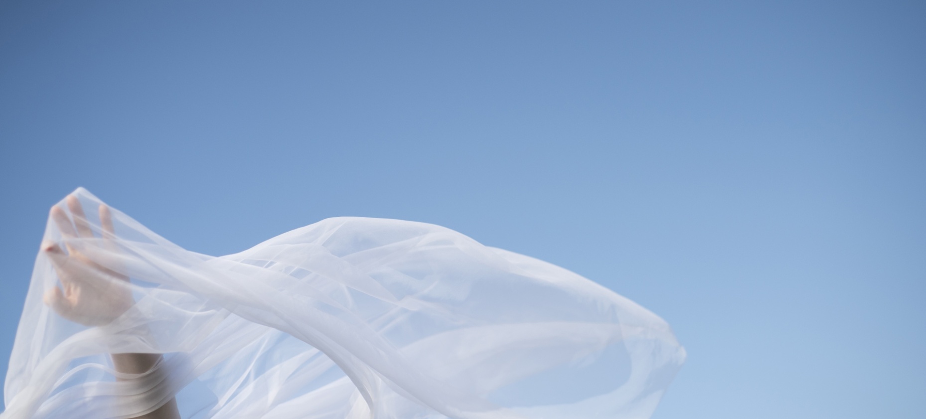 Voile blanc flottant au vent sur fond de ciel bleu, avec une main en mouvement.
