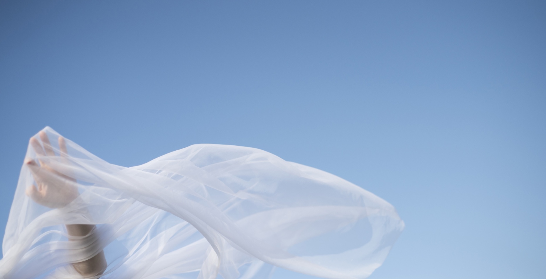 Voile blanc flottant au vent sur fond de ciel bleu, avec une main en mouvement.