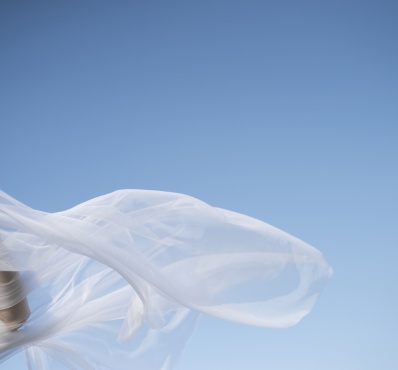 Voile blanc flottant au vent sur fond de ciel bleu, avec une main en mouvement.