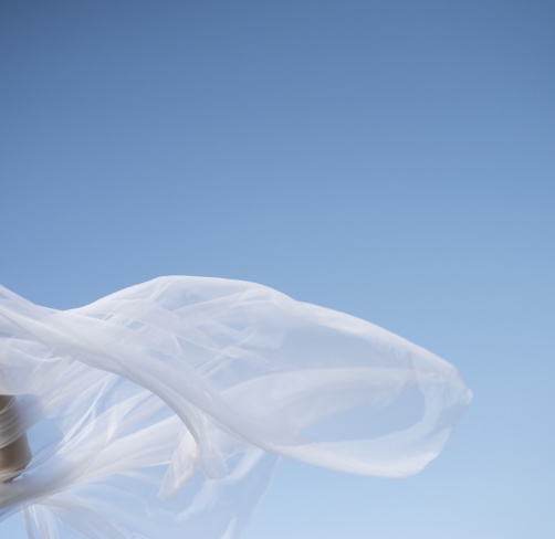 Voile blanc flottant au vent sur fond de ciel bleu, avec une main en mouvement.